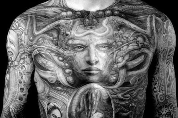 HR Giger-inspired chest tattoo with a central female face surrounded by biomechanical tubes, skulls, and surreal alien details.