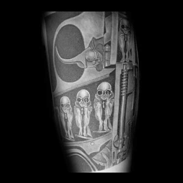 HR Giger-style tattoo showing small alien-like figures encased in a mechanical structure with surreal and biomechanical detailing.