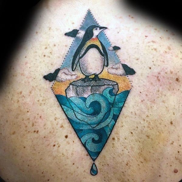 Colorful diamond-shaped tattoo of a penguin standing on ice, with swirling ocean waves, clouds, and a drop falling below.