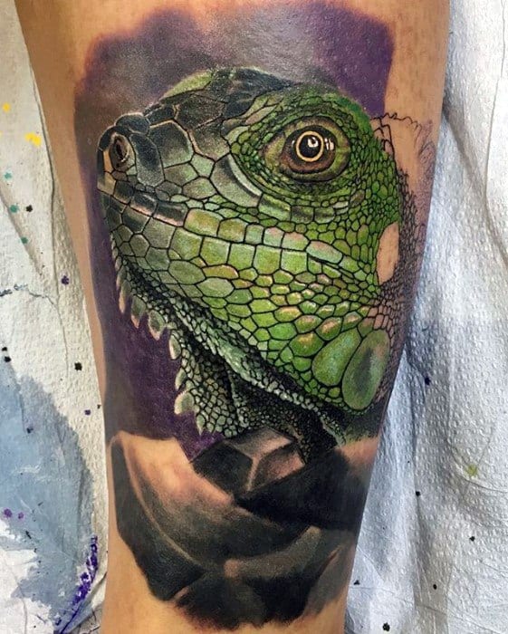 Hyper-realistic green iguana tattoo with detailed scales, vivid eye, and a soft purple and black background for contrast