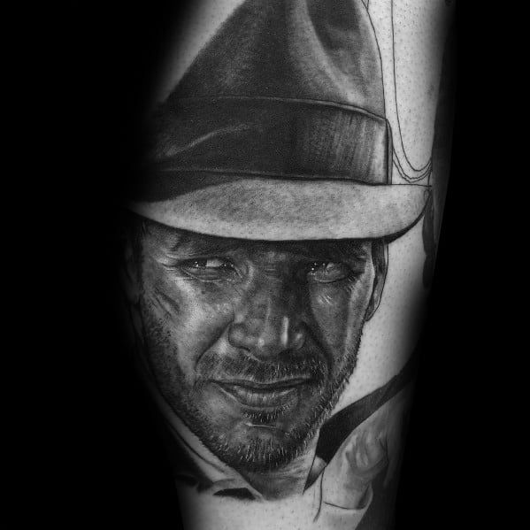 Hyper-realistic black and gray tattoo of Indiana Jones, showcasing his iconic fedora, rugged expression, and detailed shading for depth.