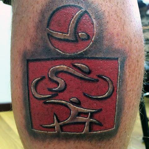 Tattoo featuring the Ironman logo with abstract representations of swimming, cycling, and running, carved in bold lines and shaded red, symbolizing the triathlon.