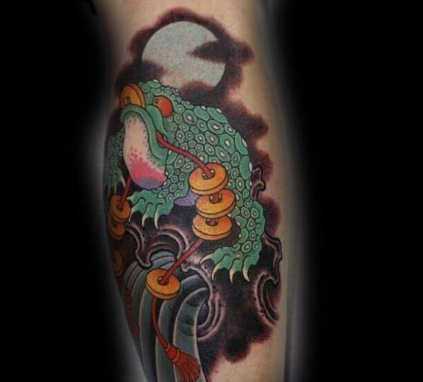Japanese-style tattoo featuring a mystical green frog adorned with gold coins, perched on a staff, set against a full moon and swirling dark clouds.