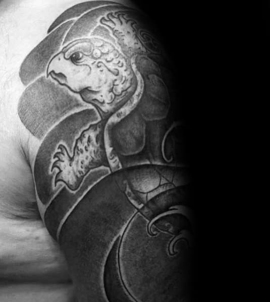 Black and grey Japanese-style turtle tattoo on the shoulder with bold shading and flowing wave elements, symbolizing longevity and strength.