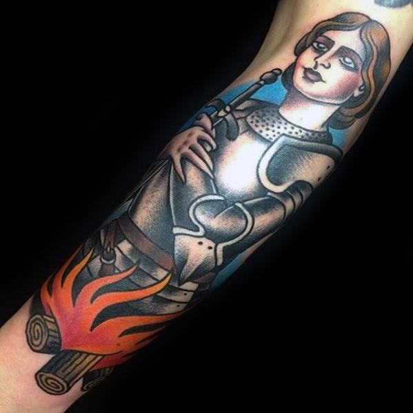 Colorful Joan of Arc tattoo on forearm showing her in armor tied to a stake, with flames below and a calm, resolute expression.
