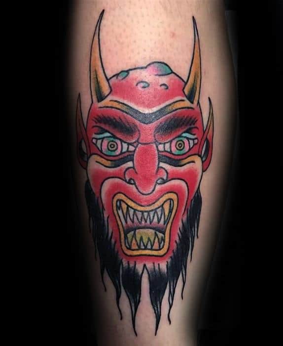 Traditional Krampus tattoo featuring a bold red demon face with sharp yellow teeth, arched brows, green eyes, and pointed yellow horns.