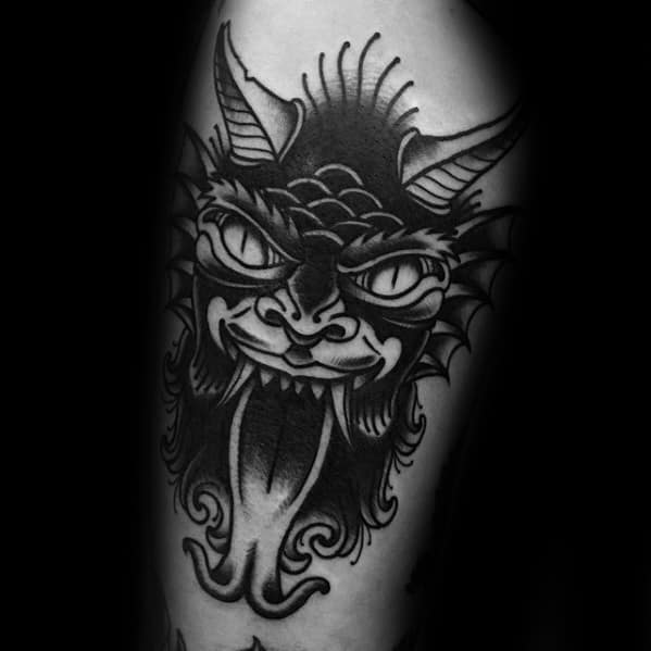 Blackwork Krampus tattoo featuring a devilish face with large eyes, coiled tongue, sharp horns, and bold line detailing for a dramatic effect.