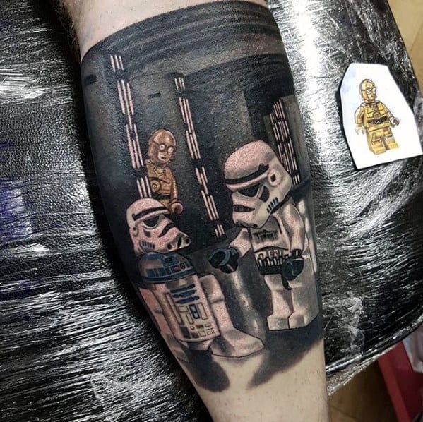 Black and grey tattoo of Lego Star Wars scene with Stormtroopers, R2-D2, and C-3PO in a Death Star corridor, featuring detailed shadows and depth.