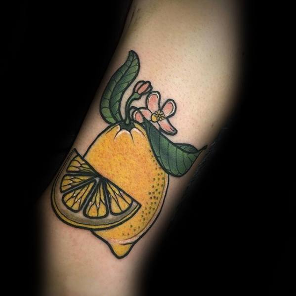 Colorful tattoo of a whole lemon with a slice, green leaves, and a pink blossom, outlined in black with vibrant, classic shading.