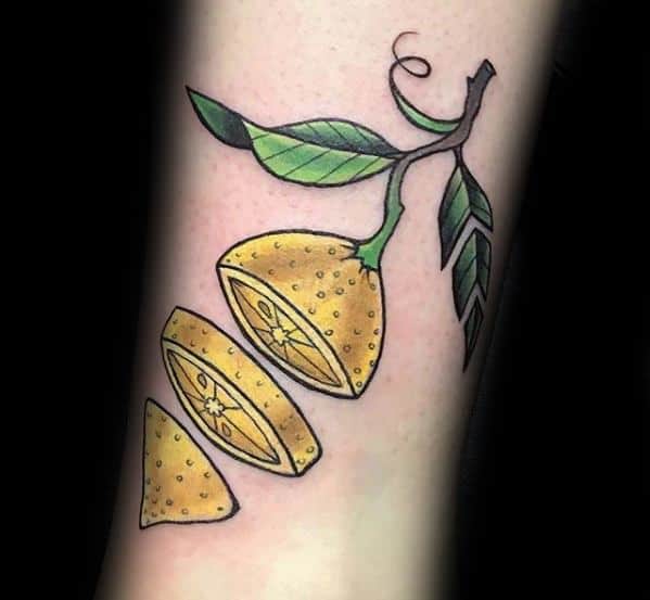 Bright and bold tattoo of a sliced lemon hanging from a branch with green leaves, each segment separated in a dynamic layout.