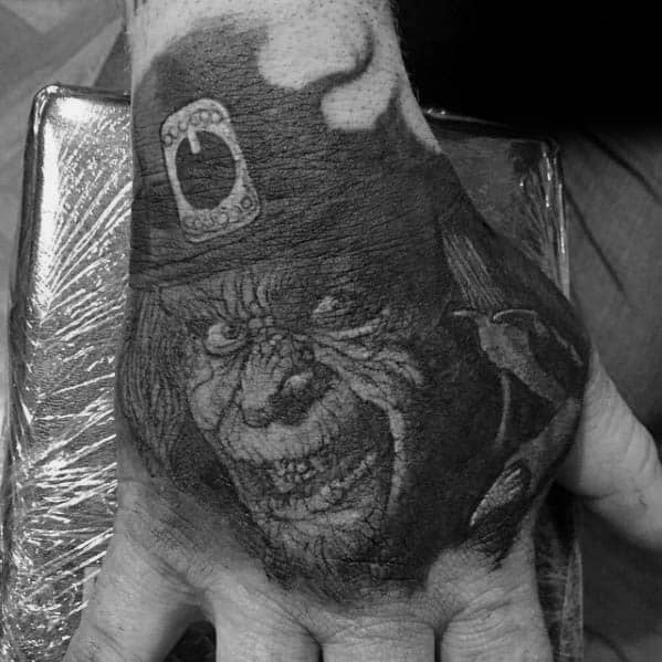 Dark and detailed blackwork tattoo on the hand of a sinister leprechaun with a menacing grin, wearing a top hat with a large belt buckle.