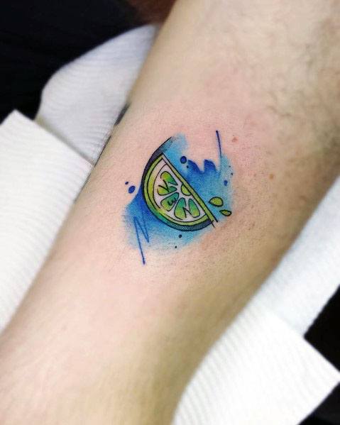 Watercolor-style lime wedge tattoo with vibrant green and yellow shading, accented by bold blue splashes for a fresh and artistic design.