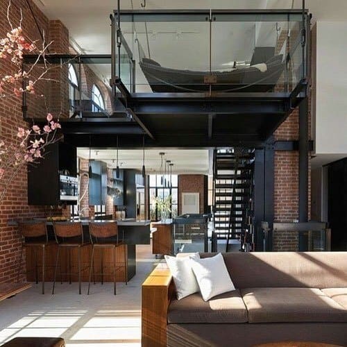 Industrial loft with brick walls, mezzanine hammock, and open kitchen with bar seating.