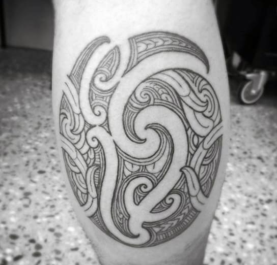 Black ink calf tattoo featuring an intricate tribal-inspired circular design with swirling patterns and fine line details