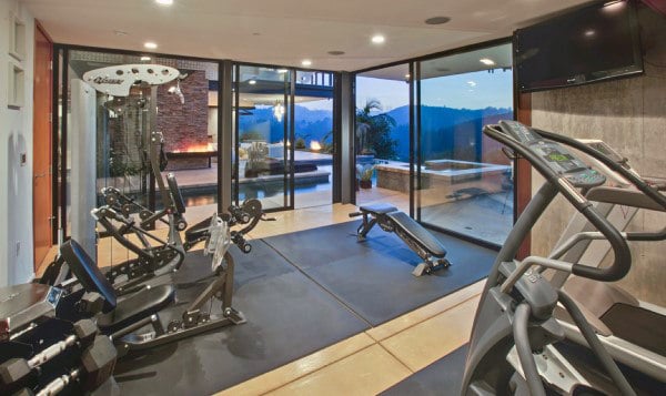 Home gym with exercise machines and a weight bench, overlooking a pool and mountain view through large glass doors