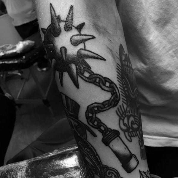 Black and gray mace tattoo featuring a spiked ball on a heavy chain with a detailed handle, symbolizing strength, battle, and resilience.