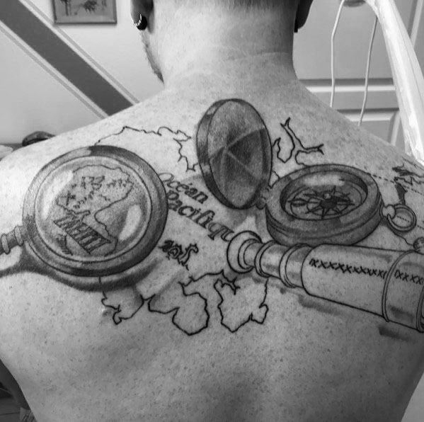 Tattoo featuring a magnifying glass, telescope, compass, and treasure map, creating a bold and adventurous exploration-themed back piece.
