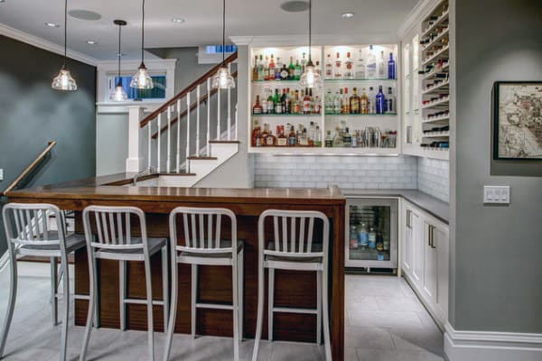 Modern basement home bar with stocked shelves, fridge, and four stylish stools