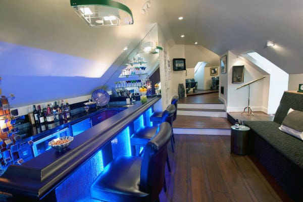Stylish bar with blue lighting, stools, and bottle shelves under a sloped ceiling