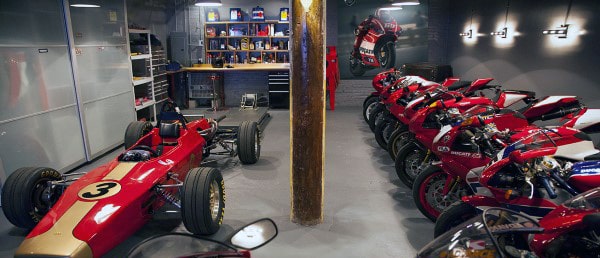 A vintage red race car and several red motorcycles are lined up in the well-organized garage