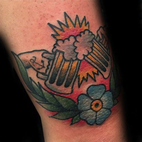 Traditional-style tattoo of two clinking beer mugs with frothy foam and a burst of yellow behind them, framed by green leaves and a blue flower for a celebratory, vintage look.