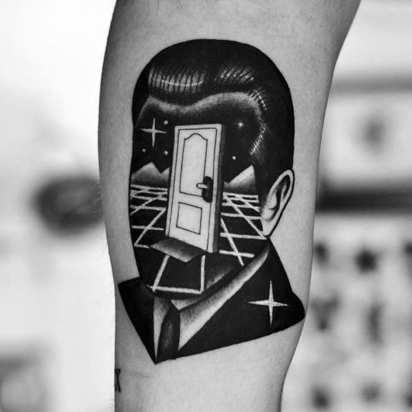 Surreal blackwork tattoo of a man in a suit with a door in place of his face, opening to a starry landscape with mountains and a grid floor.