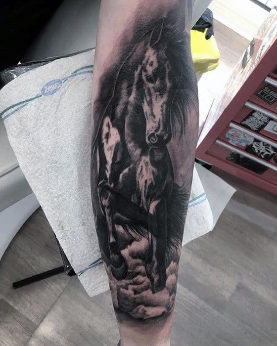 Realistic black and grey forearm tattoo of a mare and foal, featuring soft shading, cloudy textures, and gentle facial expressions