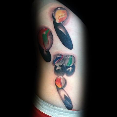 Realistic tattoo of colorful marbles with detailed shading and reflections, creating a striking 3D effect with bold shadows on the skin.