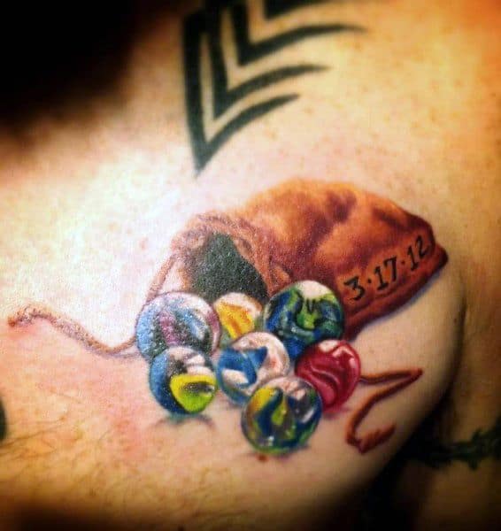 Realistic tattoo of a leather pouch spilling colorful marbles, with a date inscribed on the bag, symbolizing nostalgia and meaningful memories.