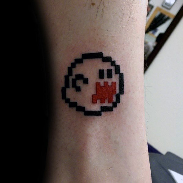 Pixelated Mario ghost tattoo featuring an 8-bit Boo with a red mouth, bold black outlines, and a retro gaming style, inked on the wrist.