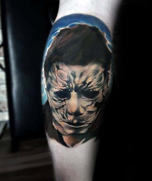 Realistic Michael Myers tattoo featuring his cracked and weathered mask, highlighted by eerie lighting for a haunting effect.
