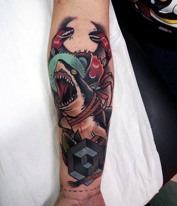 Neo-traditional forearm tattoo of a roaring shark wearing a helmet, flanked by a crab and bold geometric shapes in black and gray.