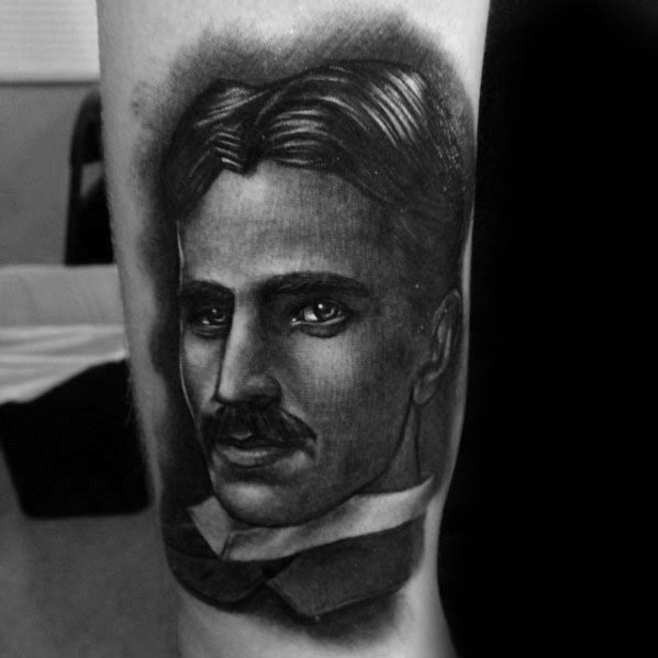 Hyper-realistic black and grey portrait tattoo of Nikola Tesla with smooth shading and intense gaze framed by soft shadowing.