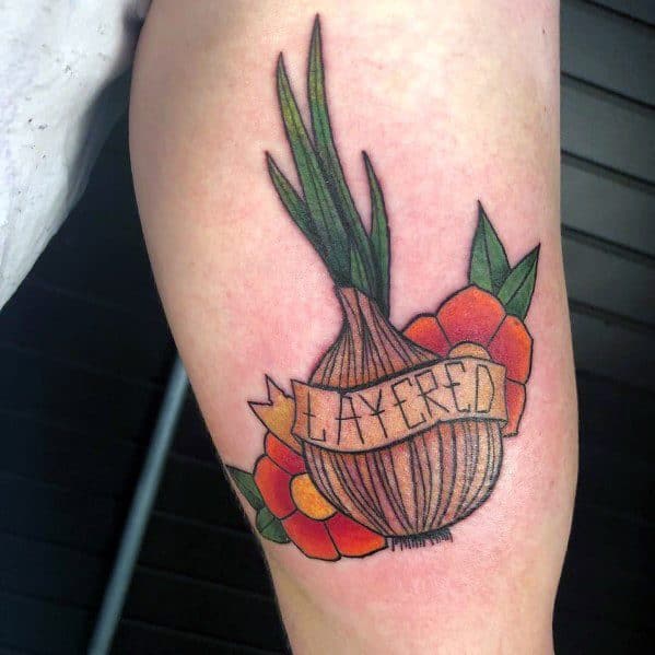 Colorful onion tattoo with a banner reading "LAYERED," surrounded by vibrant flowers and green leaves, blending traditional and illustrative styles.