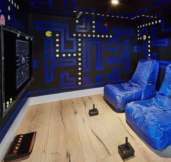 Retro gaming room with wall art and two blue chairs, featuring vintage game consoles and joysticks