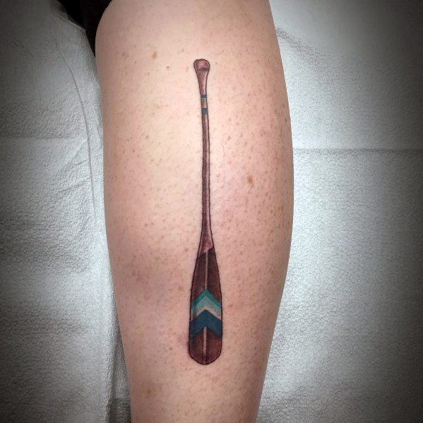 Detailed paddle tattoo on the calf with wood texture and blue chevron design, symbolizing adventure, exploration, and a love for the water.