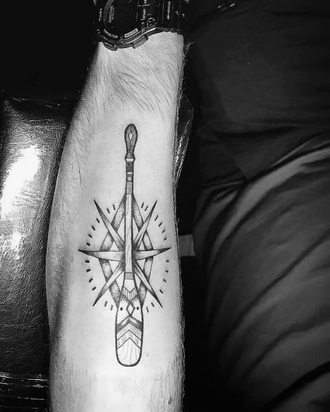 Black and grey paddle tattoo over a compass design on the forearm, symbolizing adventure, direction, and a deep connection to exploration and water.