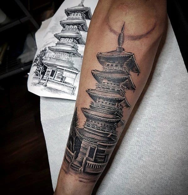 Detailed black and grey forearm tattoo of a traditional Japanese pagoda with fine linework, shading, and a faint crescent moon above.