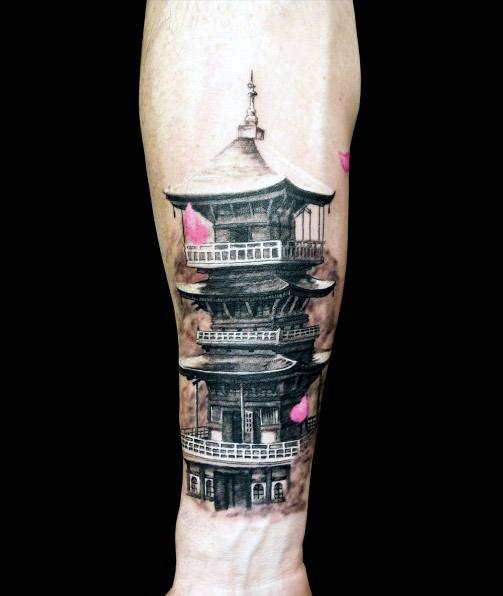 Black and grey forearm tattoo of a detailed Japanese pagoda with soft pink cherry blossom petals gently falling around it.