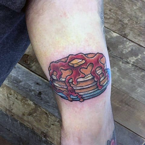 Pancake tattoo with thick dripping syrup and butter on a blue plate, featuring bold outlines and vibrant shading for a classic design.