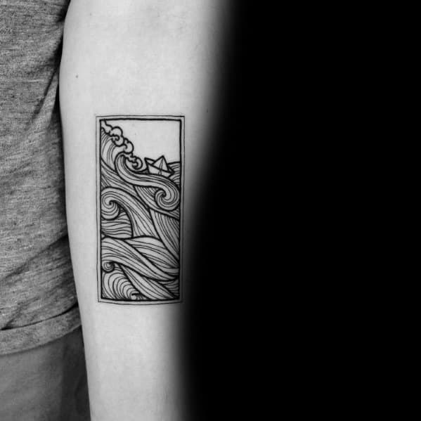 Paper boat tattoo in a rectangular frame with swirling waves, symbolizing resilience, adventure, and navigating life’s challenges.