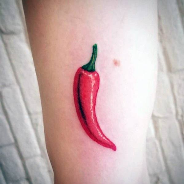 Small red chili pepper tattoo with a green stem, featuring smooth shading and a simple yet vibrant design on the arm.