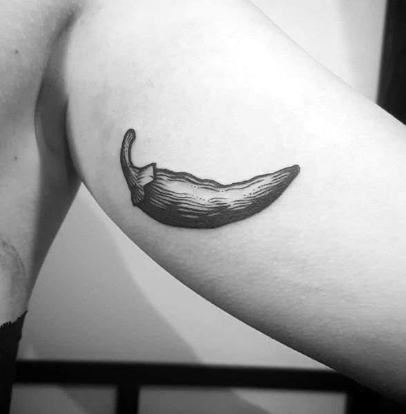 Black ink chili pepper tattoo on the upper arm with fine line shading and a rustic, hand-drawn look for a simple yet bold design.