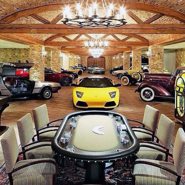 A lavish garage blending luxury cars with a poker table setup, featuring brick walls, wooden beams, and elegant chandeliers for a stylish, multifunctional space.