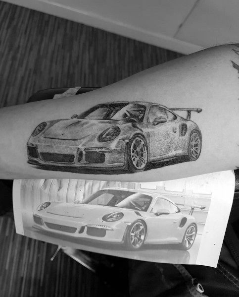 Detailed grayscale Porsche tattoo on the forearm, closely resembling the reference image below.