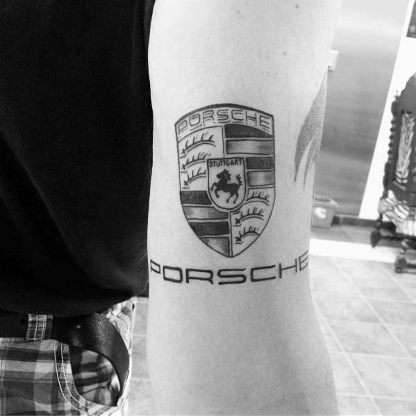 Clear black ink Porsche crest tattoo with sleek lettering beneath, placed on the upper arm.