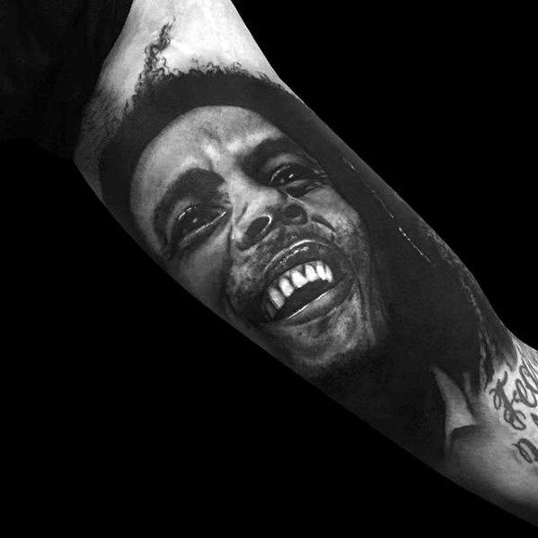 Lifelike forearm tattoo of Bob Marley with a wide smile and expressive eyes, done in bold black and gray realism.