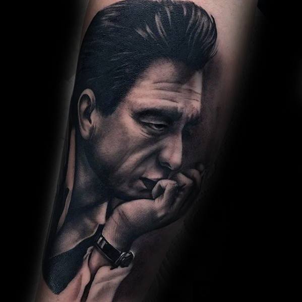 Tattoo of a thoughtful Johnny Cash with a watch, resting his chin on his hand against a dark background