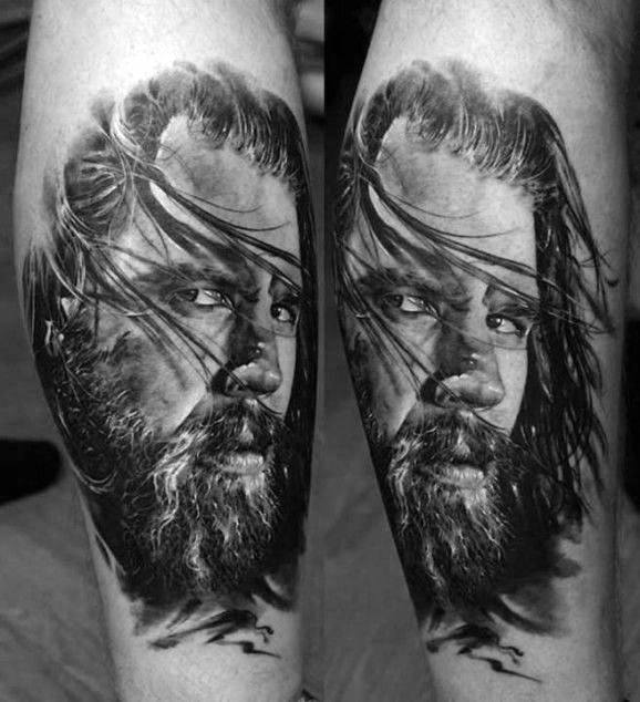 Black and gray tattoo of a man's bearded face with long hair on forearm