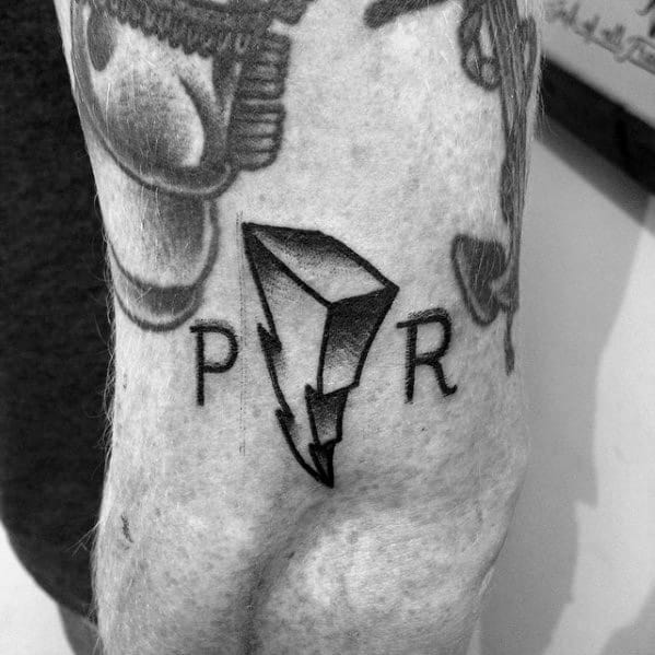 Minimalist black ink tattoo of the Power Rangers lightning bolt logo between the letters "P" and "R" on the upper arm.